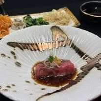 上品な白い和皿に盛り付けられた、特製ソースがかかった霜降り和牛の肉料理（前菜）