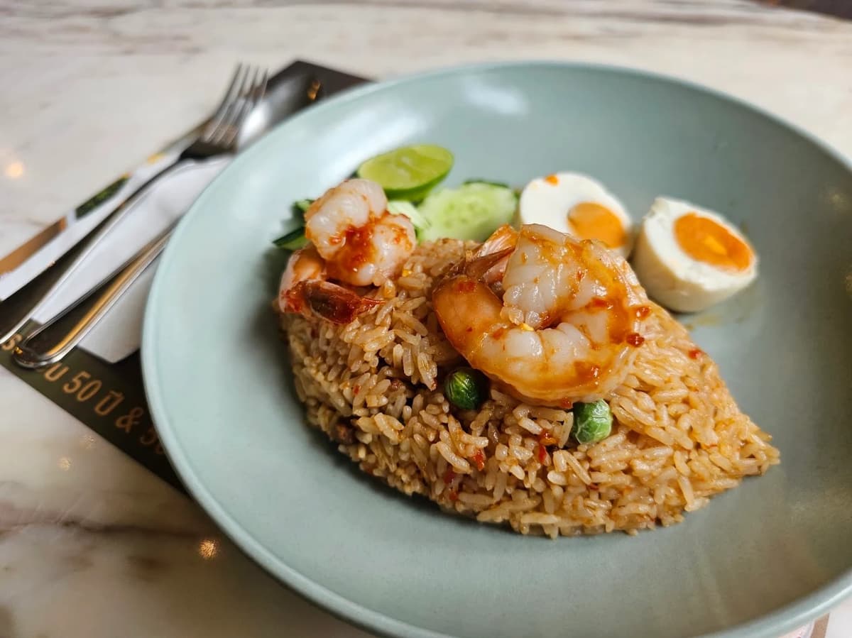 綺麗に型取られた大きなエビのチャーハン（カオパット）の皿。付け合わせにライム、キュウリ、塩漬け卵が添えられている。