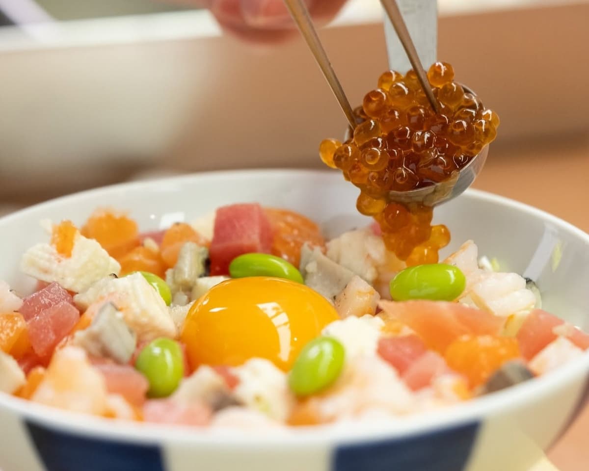 刺身や卵黄を盛り付けた海鮮丼にイクラを添える様子